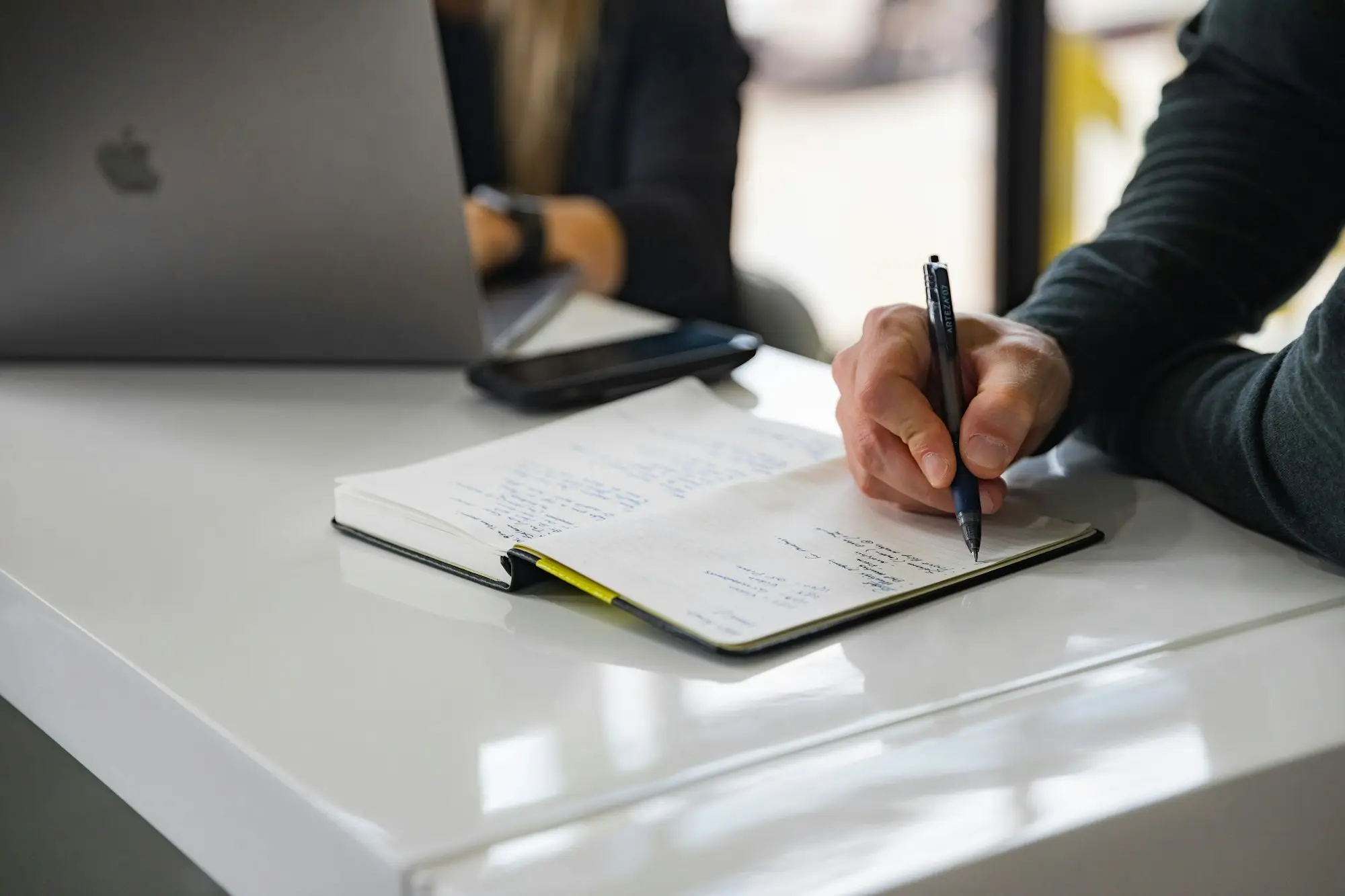 Business owner writing notes in a notebook beside a laptop