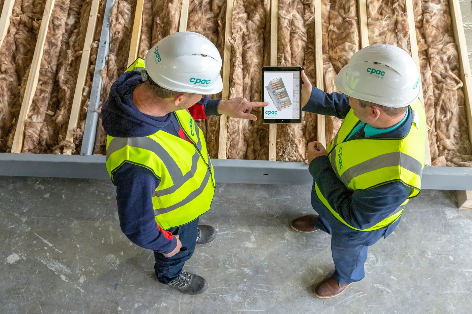 Two tradies in hi-vis checking job details on a tablet on site
